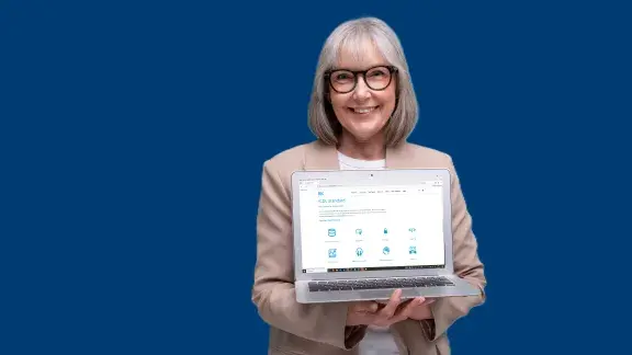 Frau mit grauen Haaren und Brille und Sakko hält einen aufgeklappten Laptop in der Hand, der Bildschirm schaut weg von ihr, man kann darauf die Website von icdl.at sehen