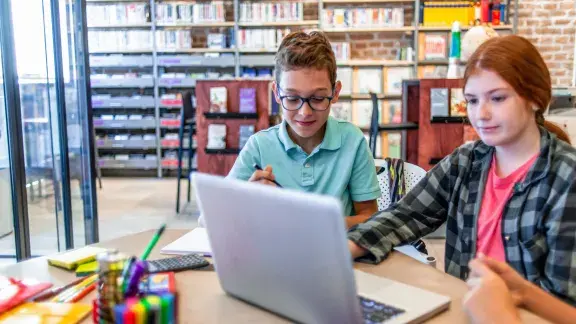 Ein Schüler und eine Schülerin vor dem Laptop in einer Bibliothek.