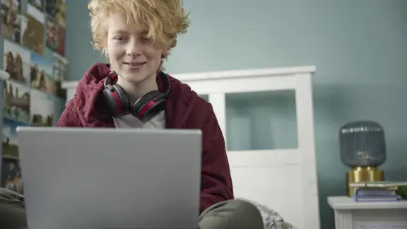 Teenage person With Wireless Headphones Working On Laptop In Bedroom At Home Stock Photo