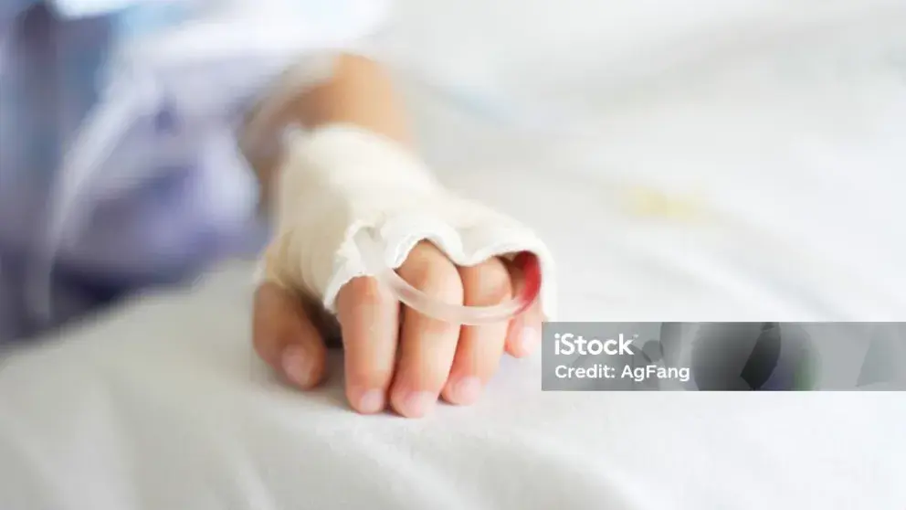 Kinderhand mit Schläuchen und Verband auf einem Krankenhausbett