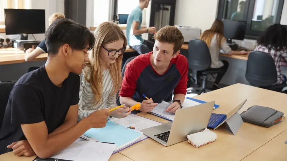Drei jugendliche Schüler*innen mit Laptops beim Lernen
