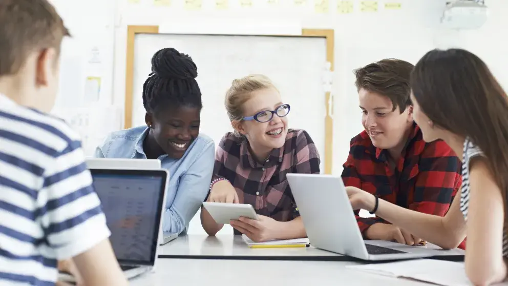 Vier Schüler*innen (ca. 10-jährig), 2 Buben, 2 Mädchen sitzen nebeneinander und schauen auf ihre Smartphones, alle tragen Schulrucksäcke