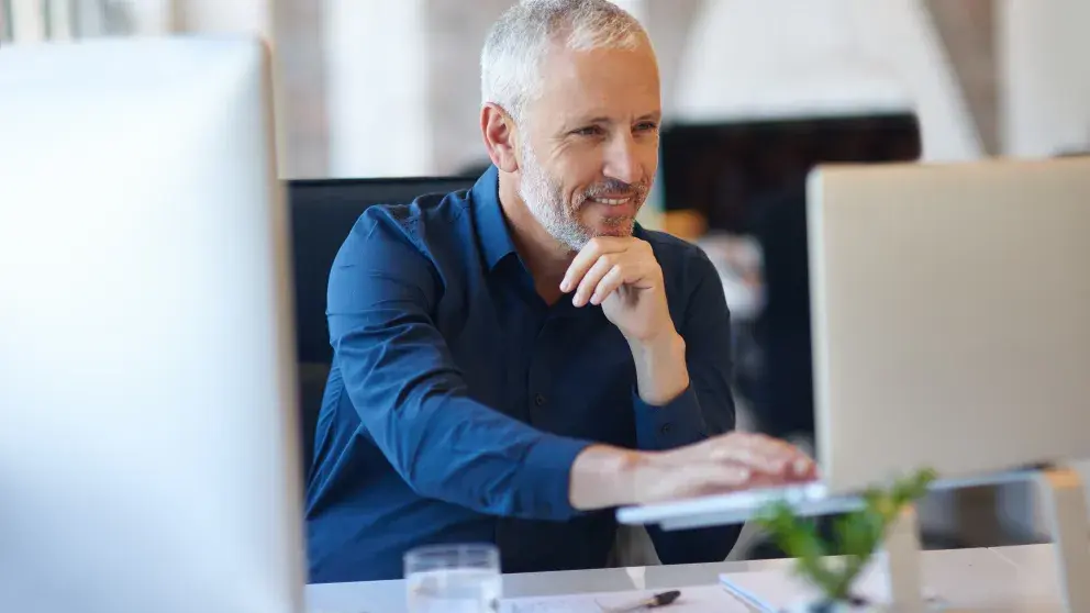 Älterer Herr schaut zufrieden auf Laptopbildschirm, modernes Büro
