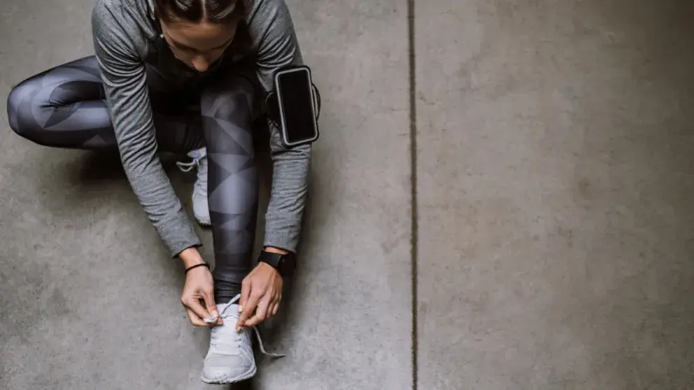 Sportliche Frau sitz am Boden und bindet sich die Sportschuhe, am Arm hat sie ein Meßgerät.