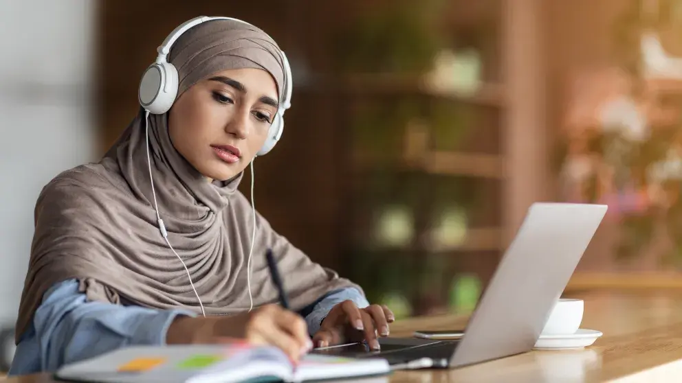 Mädchen mit Hijab nimmt Online-Unterricht am Laptop im Café, Stockfoto