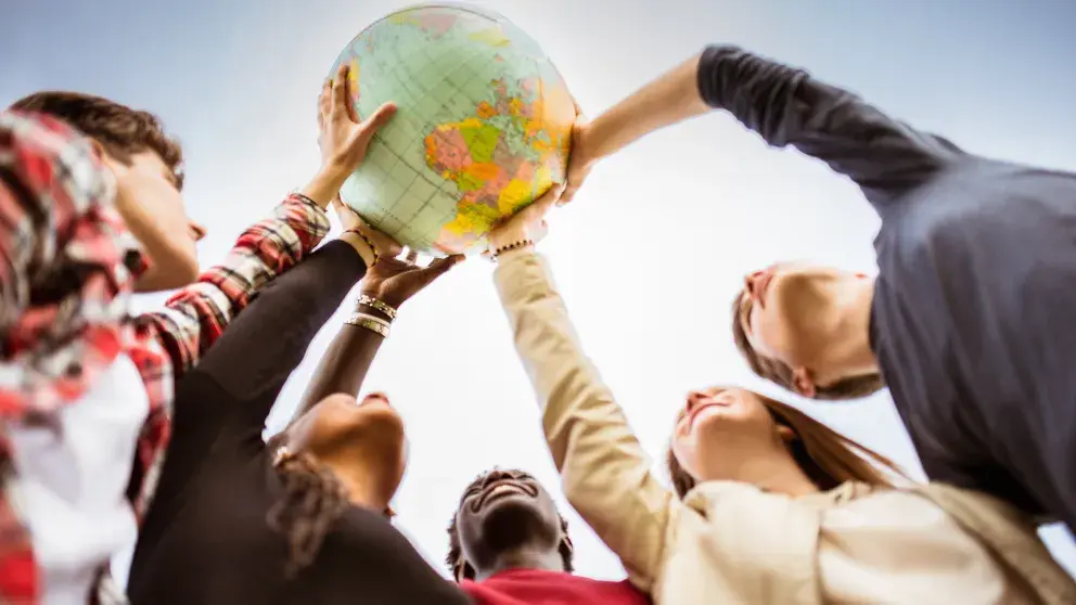 ier Menschen (jung, unterschiedliche Hautfarben) halten einen Globus gemeinsam in die Höhe