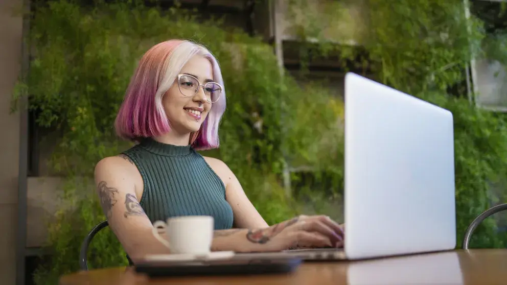 Frau mit Tattoo und rosa Haaren arbeitet in einem Café am Laptop