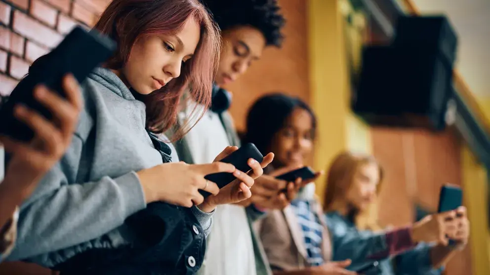 Gruppe von Teenagern mit Mobiltelefonen auf dem Flur einer High School. Stockfoto
