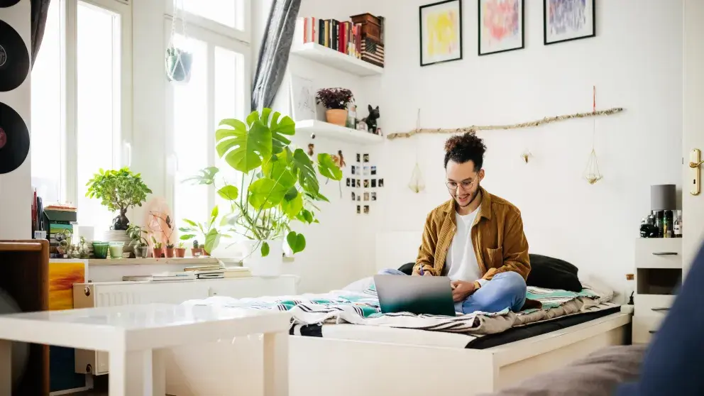 Männlicher Student studiert auf einem Bett, umgeben von Büchern und Zimmerpflanzen Stockfoto