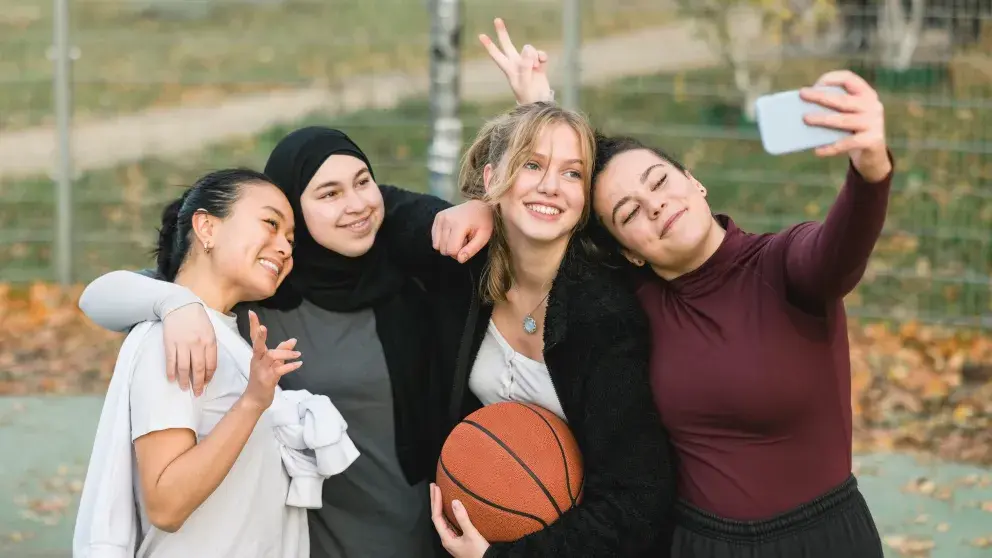Vier jugendliche Mädchen machen am Basketball Platz ein Selfie. Eine hält den Basketball in der Hand.