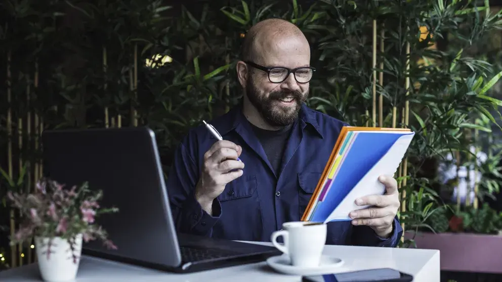 Mann mit Brille und Bart vor Laptop mit einem Block von dem er abliest