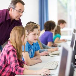 Lehrer mit Schüler*innen vor Computern